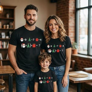 Può includere: Tre persone che indossano magliette nere abbinate con un'equazione matematica a tema natalizio stampata sul davanti. L'equazione include Babbo Natale, un albero di Natale e un regalo. Il testo recita: -9 = 7 = 4, (Babbo Natale x albero) + regalo = ?