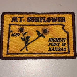 May include: A brown and yellow embroidered patch with the text "MT. SUNFLOWER HIGHEST POINT IN KANSAS" and a stylized sunflower design. The number "4039" is also included on the patch.
