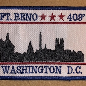 Könnte beinhalten: Gestickter Aufnäher mit weißem Hintergrund, blauem Rand und einer schwarzen Skyline-Silhouette. Der Aufnäher zeigt den Text "FT. RENO 409" über einem roten Streifen und "WASHINGTON D.C." darunter. Drei rote Sterne befinden sich über der Zahl 409.