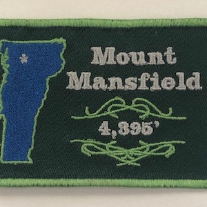 Peut inclure: Écusson brodé avec le contour bleu du Vermont et une étoile. Le texte "Mount Mansfield" est en gris, avec "4,395'" en dessous. L'écusson a un fond vert foncé et une bordure vert clair. La hauteur est d'environ 1339 mètres.