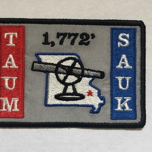 Może przedstawiać: Szara naszywka haftowana z białym obrysem stanu Missouri, czarno-białą ilustracją anteny radarowej i tekstem "1,772'" w kolorze czarnym. Tekst "TAUM" jest wyszyty na biało na czerwonym tle po lewej stronie naszywki, a tekst "SAUK" jest wyszyty na biało na niebieskim tle po prawej stronie naszywki.
