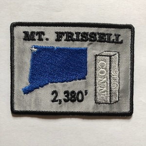 Peut inclure: Un écusson brodé gris et blanc avec le texte "MT. FRISSELL" et un contour bleu de l'état du Connecticut. L'écusson présente également une boîte blanche avec le texte "CONN" et le nombre "2 380".