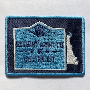 Puede incluir: Parche bordado azul y blanco con el texto "Bright Azimuth" y "47 Feet". El parche presenta una rosa de los vientos y un contorno estilizado de un faro.