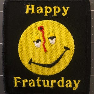 Puede incluir: Parche cuadrado negro con una carita sonriente amarilla bordada y las palabras "Happy Fraturday". La carita sonriente tiene una línea vertical roja y ojos somnolientos.