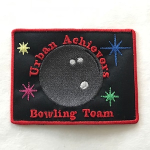May include: Black embroidered patch with red stitching. It features a bowling ball with white dots, stars in various colors, and the text "Urban Achievers Bowling Team".