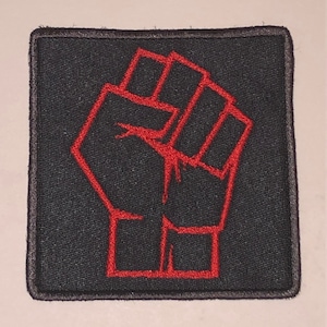 May include: A red embroidered fist raised in the air on a black fabric patch.