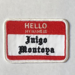 May include: Red and white name tag with the text "HELLO MY NAME IS Inigo Montoya" in black.