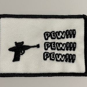 Può includere: Toppa ricamata bianca con una silhouette nera di una pistola giocattolo e il testo "PEW!! PEW!! PEW!!"