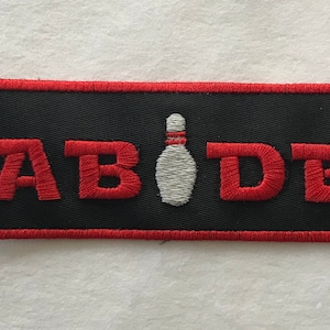 May include: Black embroidered patch with red stitching and the word "ABIDE" in red letters. A white bowling pin is centered between the letters.