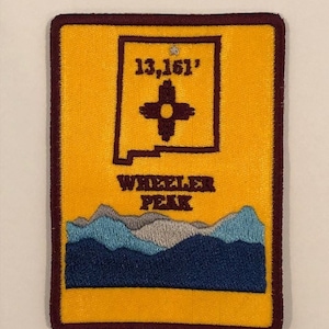 Może przedstawiać: Żółta naszywka haftowana z bordową obwódką. Naszywka przedstawia stylizowany zarys stanu Nowy Meksyk z tekstem "13,161'" i stylizowanym symbolem Zia wewnątrz. Pod zarysowaniem stanu znajduje się tekst "WHEELER PEAK" i stylizowany pasmo górskie.