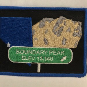 Puede incluir: Un parche bordado en negro y azul con una cordillera y un cartel verde que dice "Boundary Peak Elev 13,140".
