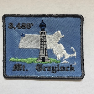 May include: A blue embroidered patch with a white outline of the state of Massachusetts, a lighthouse, and the text "3,489' Mt. Greylock".