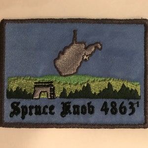 May include: Blue embroidered patch with a gray outline. The patch features a gray outline of the state of West Virginia with a white star in the center. Below the state outline is a green field with a small gray structure and a black inscription that reads "Spruce Knob 4863'"