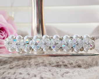 May include: A white hair clip with iridescent flower-shaped beads and pearls.