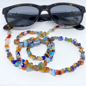 A colorful beaded strand with lots of orange, red, yellow, light and dark blues sits in front of a pair of sunglasses.