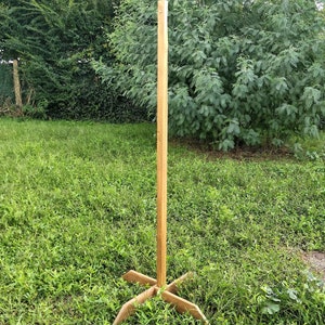 Op de afbeelding: Een houten standaard met een hoge, verticale paal en een vierpuntige basis. De standaard is gemaakt van natuurlijk hout en staat op een gazon.