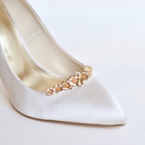Peut inclure: Chaussures de mariée en satin blanc avec un ornement floral doré sur l'orteil.