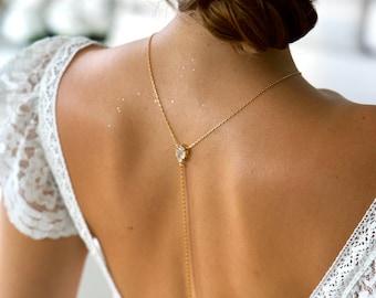 May include: A white lace dress with a gold chain back detail featuring a crystal pendant.
