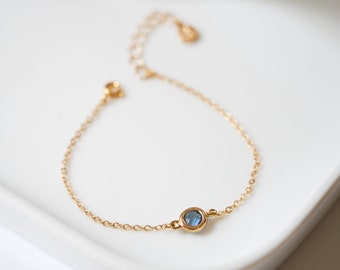 May include: A delicate gold chain bracelet with a single blue gemstone.