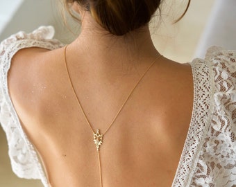 May include: A woman wearing a white lace dress with a gold back necklace featuring a delicate floral design.