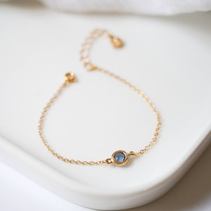 May include: A delicate gold chain bracelet with a single blue gemstone.