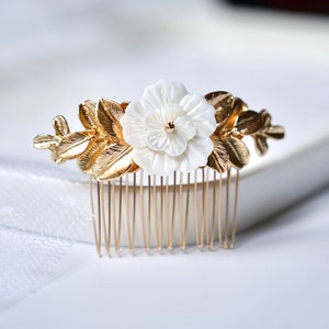May include: Gold hair comb with a white flower and gold leaves. The comb has a row of gold teeth.
