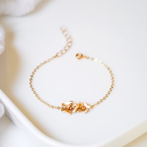 May include: A delicate gold chain bracelet with a floral design. The bracelet features a cluster of small, gold flowers.