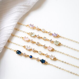 May include: Five gold chain bracelets with different colored gemstones. Each bracelet features a delicate chain with small clear stones and larger pear-shaped stones in shades of blue, pink, and green.