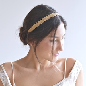 Puede incluir: Una mujer con un vestido blanco y una diadema dorada. La diadema está hecha de una serie de pequeños círculos conectados.