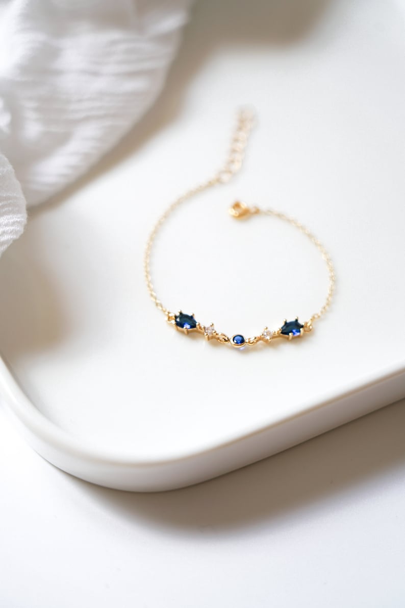 May include: A gold chain bracelet with blue and clear gemstones. The bracelet has a delicate design and is perfect for everyday wear.