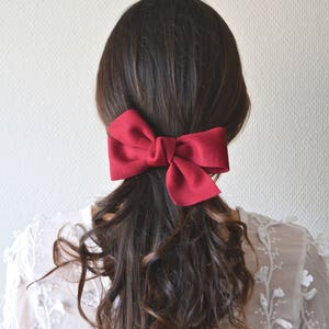 May include: A woman with long, dark brown, curly hair is wearing a red fabric bow in her hair.