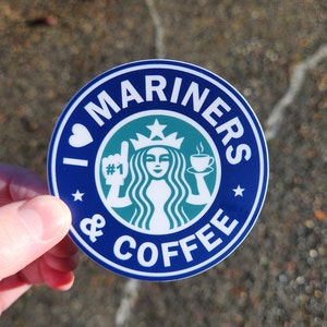 May include: A blue and green round sticker with the text "I love Mariners & Coffee" and a stylized Starbucks logo with a woman holding a cup of coffee. The text "#1" is on the woman's glove.
