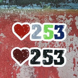 May include: Two stickers with a heart and the number 253. The top sticker has a red heart with a textured pattern and the numbers are gray, green, and blue. The bottom sticker has a brown heart and the numbers are black.