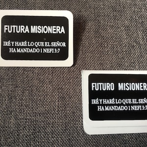以下が含まれることがあります： 丸みを帯びた角を持つ2つの白い長方形のカード。それぞれ黒い背景に黒いテキストが書かれています。テキストは「FUTURA MISIONERA」と「FUTURO MISIONERO」で、下に聖書の詩があります。カードは灰色のテクスチャのある表面にあります。