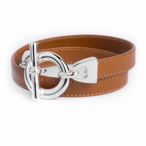 May include: A brown leather wrap bracelet with a silver toggle clasp. The clasp is a large, round ring with a bar that goes through it.