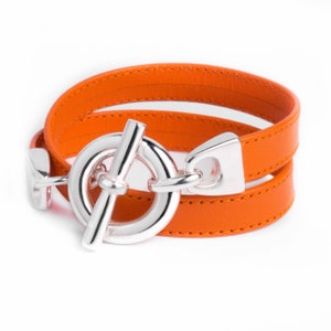 Peut inclure: Un bracelet en cuir orange à double tour avec une fermeture à boucle argentée.