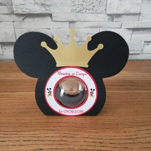 Peut inclure: Oreilles de Mickey Mouse noires et blanches avec une couronne dorée sur le dessus. Les oreilles ont un cercle rouge avec une tête de Mickey Mouse à l'intérieur et le texte "Bapteme de Cuirpo le 01.06.2019".
