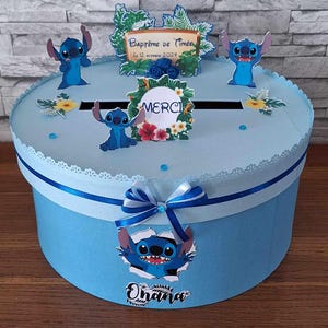 Peut inclure: Une boîte à cadeaux bleue et blanche sur le thème du personnage Stitch. La boîte a une fente pour les cartes et les enveloppes. La boîte est décorée de fleurs, de feuilles et du texte "Bapteme de Timeo le 12 octobre 2021" et "Merci".