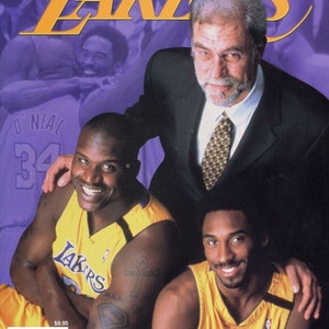 Op de afbeelding: Een tijdschriftcover met de NBA-wereldkampioenen van 2000, de Los Angeles Lakers. De cover toont drie spelers: Shaquille O'Neal, Kobe Bryant en Phil Jackson. De tijdschriftcover is paars met gele tekst die "2000 NBA World Champions Lakers" luidt.