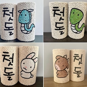 May include: Four cylindrical vases with a textured, off-white surface. Each vase features a different cartoon animal illustration in black and various colors, including a dragon, turtle, bunny, and horse. Korean text is also present on each vase.