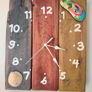 Può includere: Un orologio in legno rustico con numeri e lancette bianchi. L'orologio è composto da tre pezzi di legno, ognuno dipinto di un colore diverso: marrone, rosso e verde. Una conchiglia è attaccata al lato sinistro dell'orologio. Un infradito è attaccato al lato destro dell'orologio.