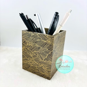 Peut inclure: Un porte-stylos noir et or avec un motif de vagues. Le porte-stylos est rempli de stylos et de crayons.