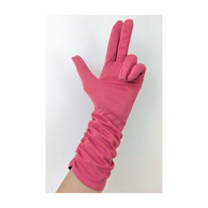 May include: A single, long, pink glove with a ruched design on the forearm. The glove is made of a smooth material and is shown with the fingers extended in a gesture against a white background.