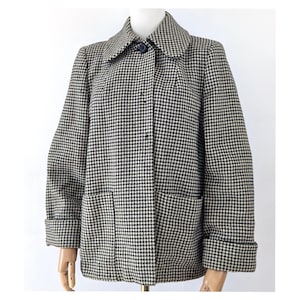 May include: A black and white houndstooth patterned jacket featuring a wide collar, long sleeves with folded cuffs, and two large front patch pockets. The jacket is secured with a single visible dark button at the neckline and a hidden button placket.