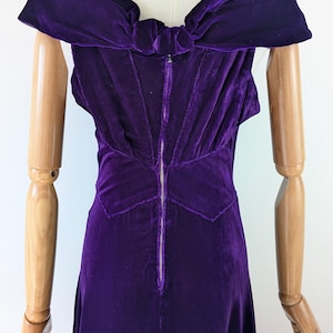 May include: A vintage, sleeveless, purple velvet dress. The dress features a bow detail at the back and a full-length zipper. The dress is displayed on a mannequin.