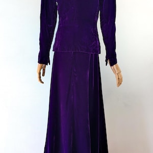 May include: A vintage, two-piece, purple velvet suit. The jacket has long sleeves and a tailored fit, paired with a matching floor-length skirt. The rich color and luxurious fabric suggest a formal or evening wear ensemble.