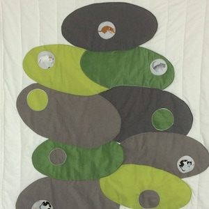 Peut inclure: Une courtepointe blanche avec une pile de formes de tissu vertes et brunes. Chaque forme a un petit cercle avec une image de chat à l'intérieur.