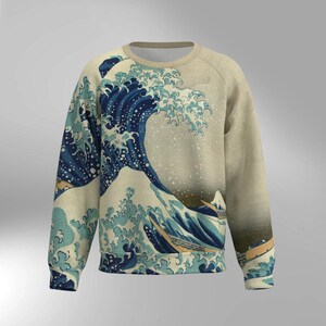 May include: A beige sweatshirt featuring a print of the iconic Japanese artwork "The Great Wave off Kanagawa." The design showcases a large, stylized wave in shades of blue and white, with a mountain in the background. The sweatshirt has a crew neck and long sleeves.