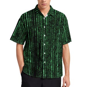 Op de afbeelding: Een zwart en groen overhemd met korte mouwen en knopen met een herhalend patroon van groene code op een zwarte achtergrond.