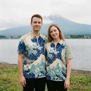 May include: Two people wearing matching polo shirts with a wave design in blue and cream. The shirts have a collared neckline and a zip. The background shows a lake and a mountain.